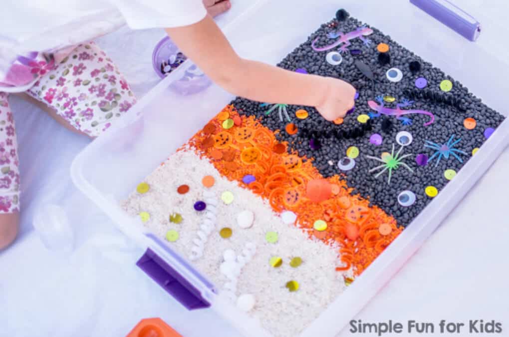 Halloween sensory bin showing a child playing with orange, purple and white rice and beans