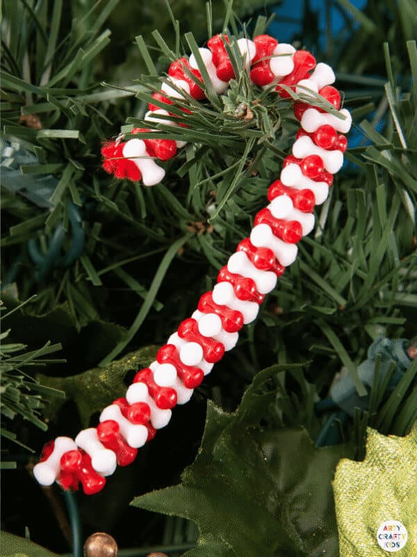 nopin="nopin" White and red beaded candy cane ornament hanging from Christmas tree