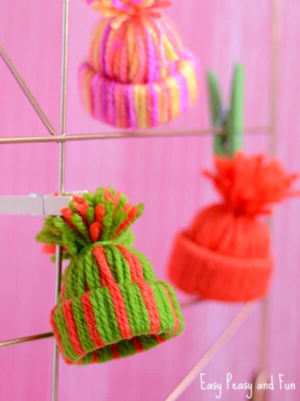 nopin="nopin" mini hat ornaments for Christmas made with yarn hanging in a pink background