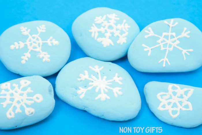 nopin="nopin" light blue painted stones with a white snowflakes drawings
